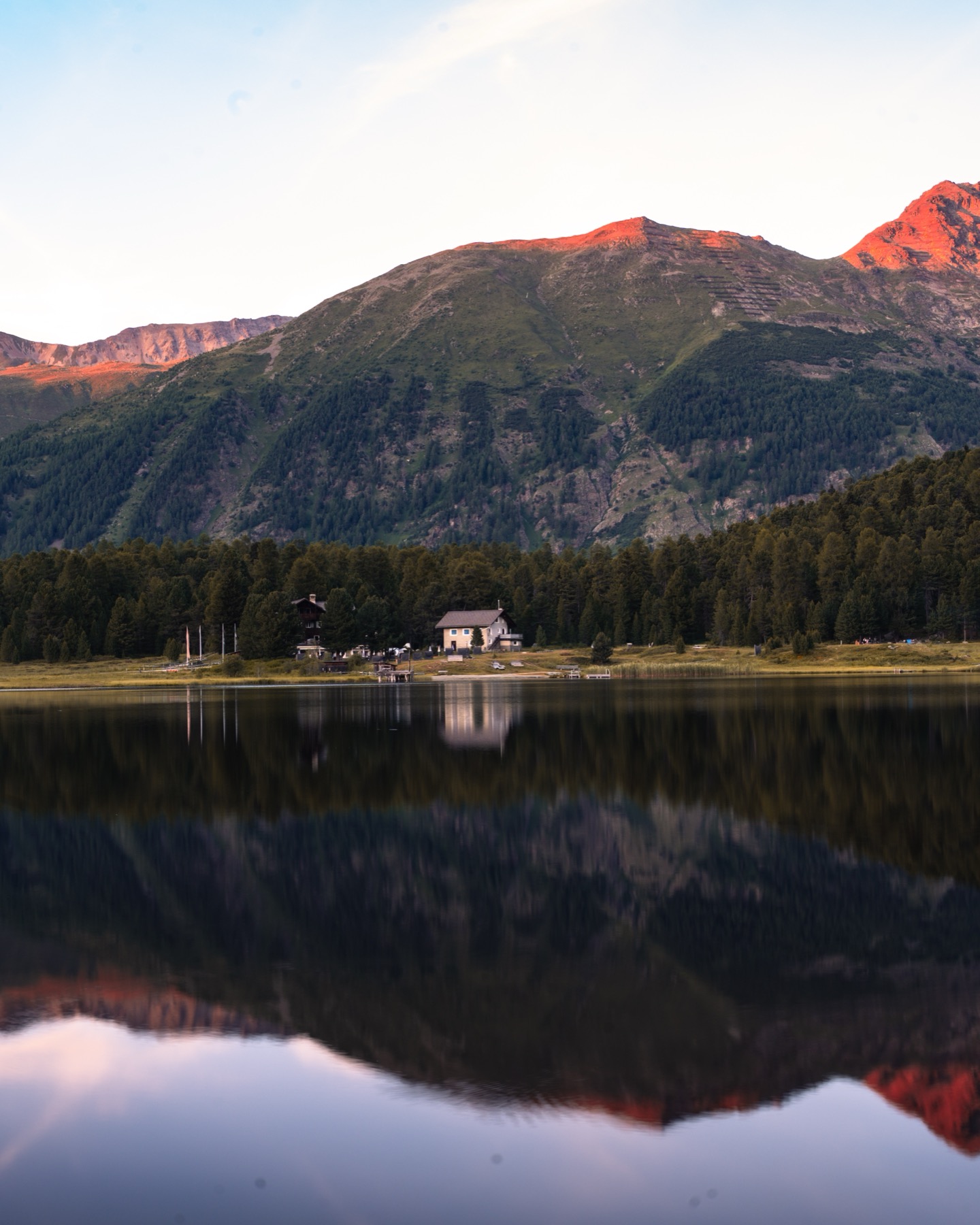 Alpenglow on the mountains reflected in a still Engadin lake