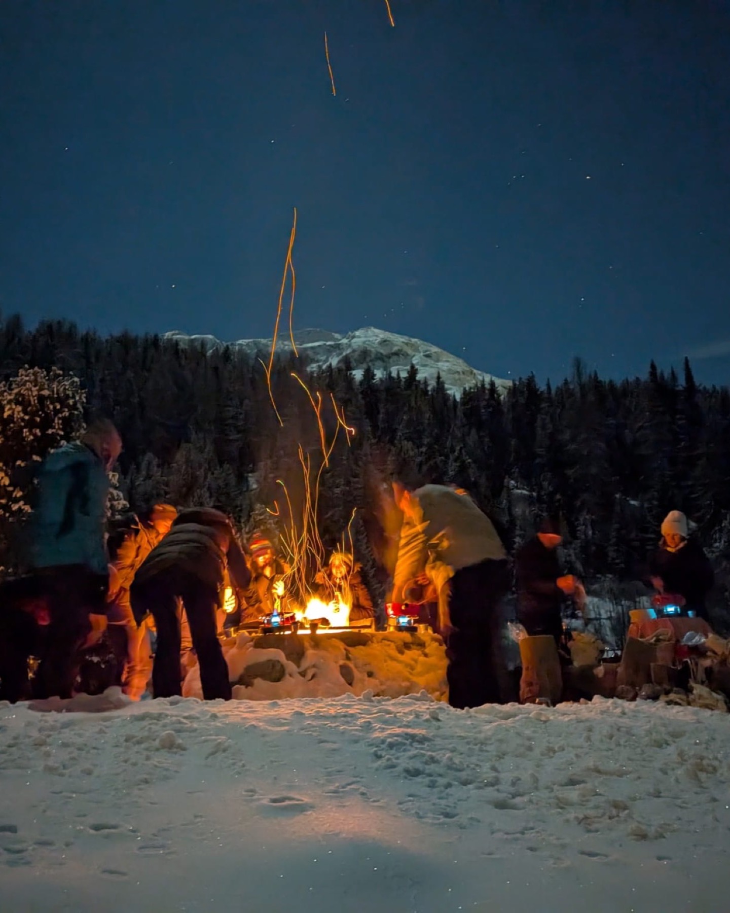 Friends gathered around a snow campfire at night in the mountains